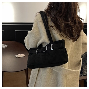 Close-up of black suede shoulder bag with retro metal buckles on beige coat