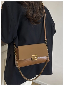 Close-up of a brown shoulder bag with mixed leather textures and vintage gold buckle