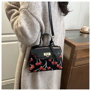 Detail of a chic cherry print shoulder bag with gold twist lock on a knit sweater model
