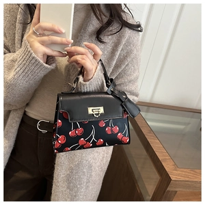 Detail of black cherry print handbag with golden twist lock and elegant top handle