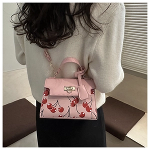 Pink shoulder bag with red cherry print featuring a silver metal buckle and top handle