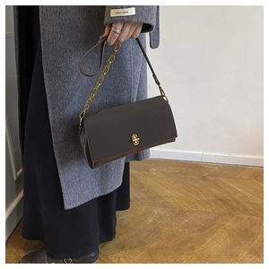 Detail of dark brown leather shoulder bag featuring a gold geometric twist-lock and chain strap