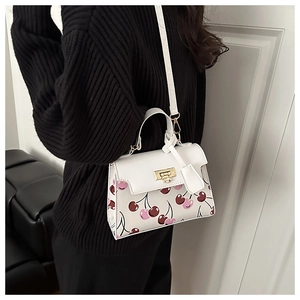 Detail view of cherry print handbag with gold heart buckle on white leather material