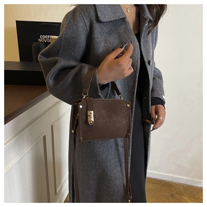 Detail of brown leather handbag with gold square buckle worn with a grey wool coat
