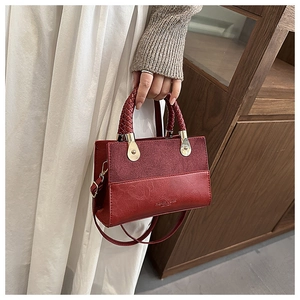 Detail van bordeauxrode patchwork handtas met geweven handvat en reliëflogo op leer