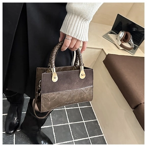Detail van vintage tas met bruin patchwork, geweven handvat en gouden hardware