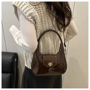 Detail of a dark brown patent leather crossbody bag with gold rotating square lock clasp