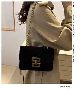 Close-up of black velvet quilted crossbody bag with gold chain strap on a trench coat
