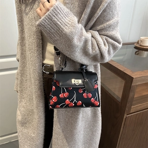 Retro black PU leather handbag with red cherry print and gold chain strap in cafe setting