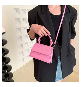 Pink faux crocodile leather mini bag with knot handle worn by a model in a black suit