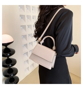Close-up of cream crocodile pattern shoulder bag with knot handle and metal strap buckle
