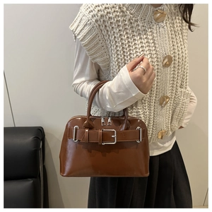 Detail of a brown leather handbag with decorative buckle and dual top handles