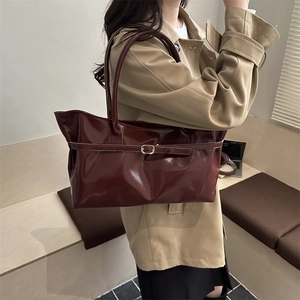Glossy burgundy leather tote bag with gold buckle detail worn with a trench coat