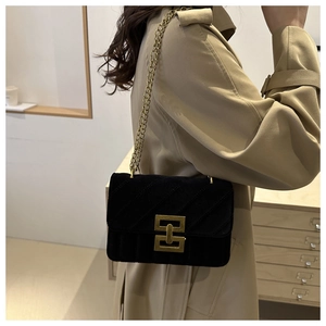 Close-up of black velvet quilted handbag with gold chain strap and geometric metal buckle