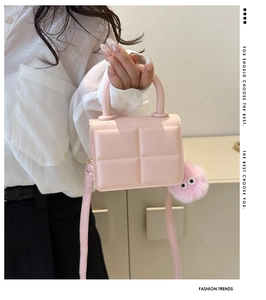 Detail of pink quilted square handbag with plush ball charm and slender shoulder strap
