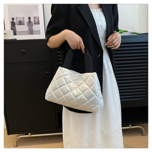 Detail of silver quilted tote bag featuring metallic finish and black top handles
