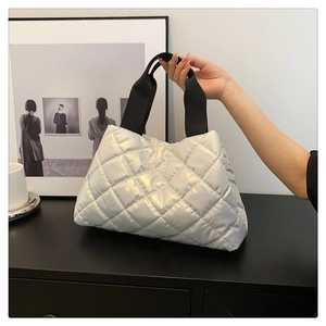 Detail of silver quilted puffer bag with glossy metallic finish and black woven handle