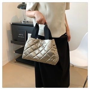 Close-up of golden quilted puffer bag featuring metallic sheen and wide fabric handles