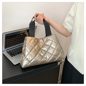 Detailed macro view of champagne gold quilted tote bag with black handles in office setting