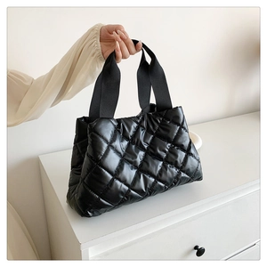 Detail of quilted black nylon tote bag with glossy finish and wide webbing straps