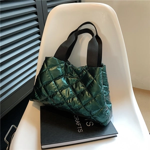 Detail of glossy quilted dark green tote bag with wide black woven straps on a chair