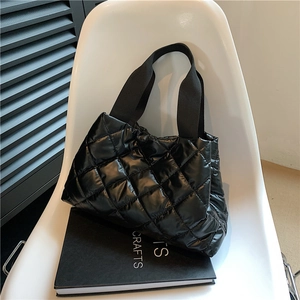 Detail view of black quilted puffer handbag with glossy finish on a modern white chair