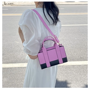 Detailed side view of pink and black color-block handbag worn with white dress