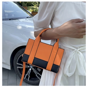 Detailed side view of orange and black contrast PU leather crossbody bag held by model