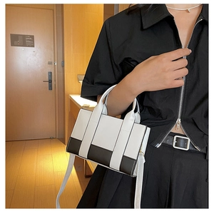 Detail of color-block tote bag with top handles and white shoulder strap on a model