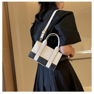 Detail of a structured black and white contrast handbag with gold hardware on a model