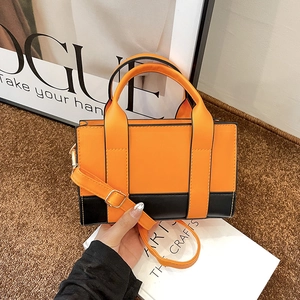 Detail view of a contrasting orange and black handbag with gold hardware and shoulder strap