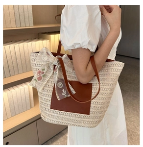 Detail of woven straw tote bag featuring leather handles and pink floral lace bow