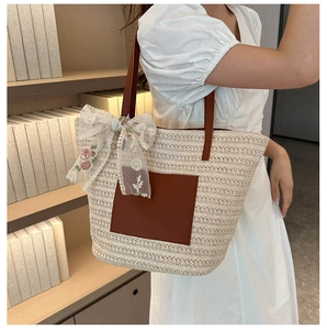 Close-up of woven tote bag with brown leather pocket and floral lace bow charm