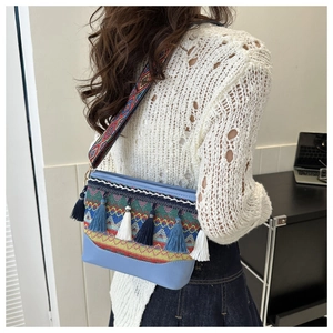 Close-up of ethnic shoulder bag featuring blue leather, colorful tassels and woven strap