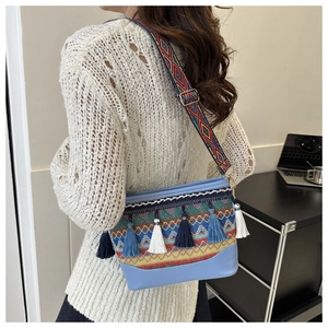 Close-up of ethnic crossbody bag with geometric embroidery, tassels, and wide woven strap