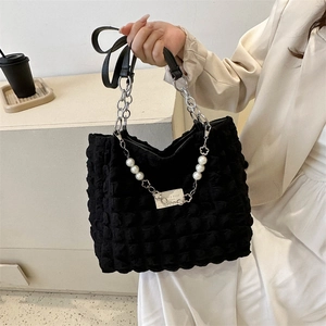 Sac fourre-tout noir à texture bulle avec chaîne perlée et bandoulière sur bureau épuré
