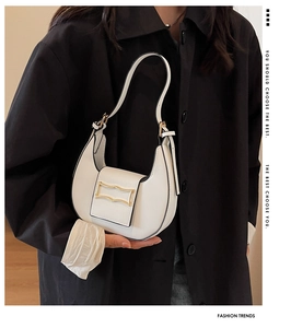 Close-up of white leather hobo bag with gold metal buckle worn with a black coat