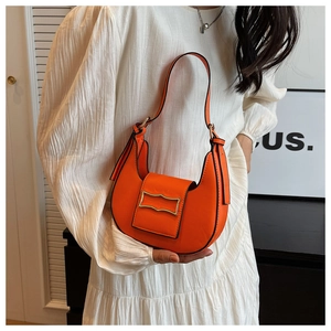 Chic orange hobo shoulder bag with a gold buckle worn with a beige textured dress