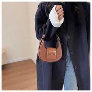 Brown leather half-moon shoulder bag with gold arch buckle shown on a model