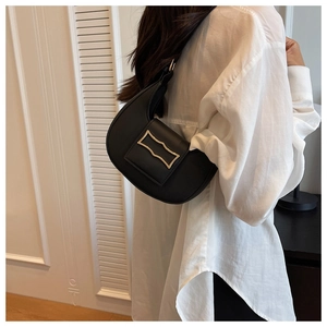 Detail of black half-moon shoulder bag with unique gold buckle worn over a white shirt