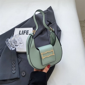 Detail of mint green half-moon hobo bag with a wavy gold buckle on a grey blazer