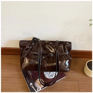 Détail de sac porté épaule en cuir verni marron avec boucle argentée sur bois