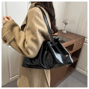 Side view of a black pleated PU tote bag with glossy finish on a female shoulder