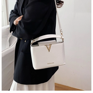 Close-up of white leather bucket bag with gold V-decoration and fashion lettering
