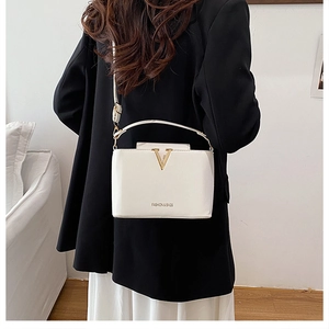 Detail of white box bag with gold V-decoration and adjustable shoulder strap