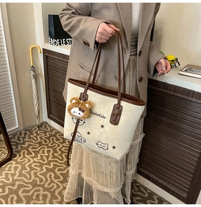 Detail van beige shopper met bruine bies en pluchen beerhanger bij een model