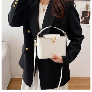 Detail of white leather crossbody bag featuring gold V-logo and fashion typography