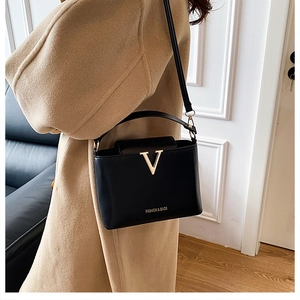 Detail of black bucket bag featuring golden V-shaped hardware and fine leather texture