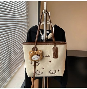 Detail van een crème en bruine shopper met kattenborduurwerk en een pluchen kattenhanger
