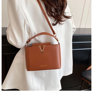 Brown leather bucket bag with gold V hardware worn by model in white suit blazer